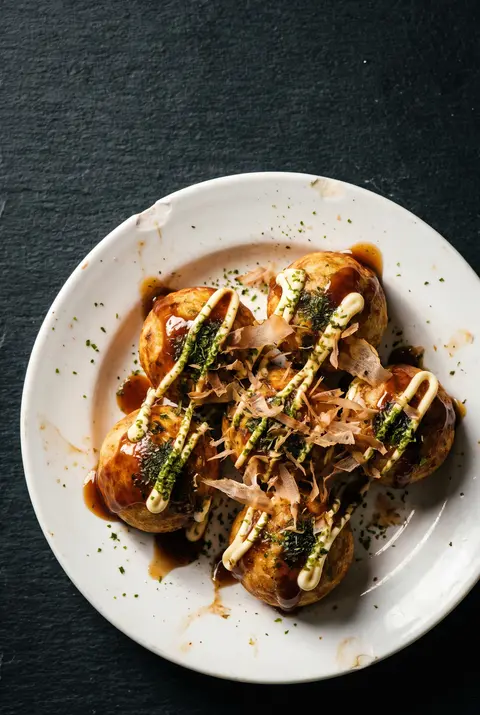 Six takoyaki balls with brown sauce on a white plate