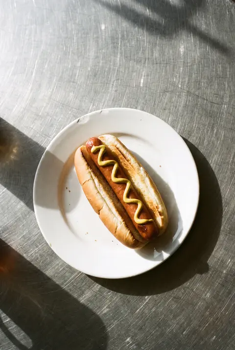 A hot dog in a soft bun with mustard on a white plate