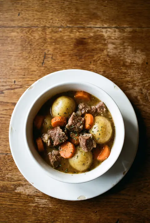 A white porcelain bowl of Irish stew with lamb on a white plate