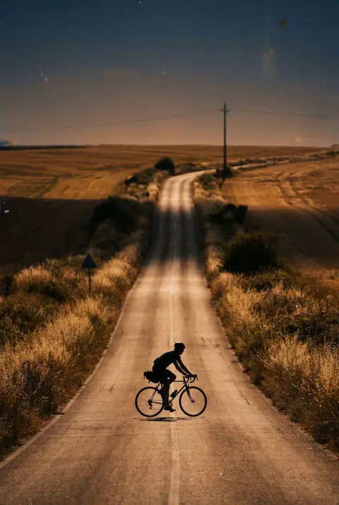 One cyclist on a plain steel road bike on an empty country road