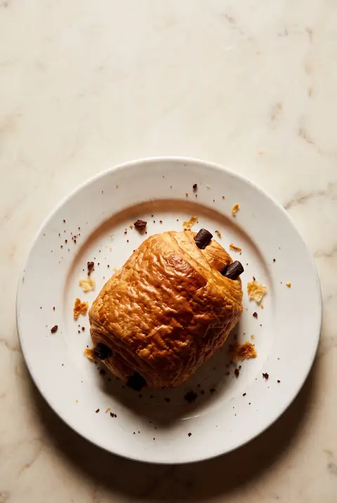 A flaky pain au chocolat with two dark chocolate edges showing on a white plate