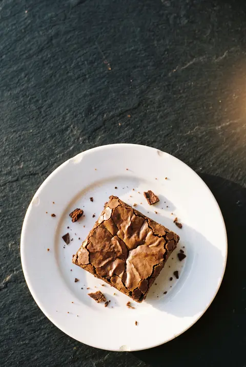 A square chocolate brownie with a crackly top on a white plate