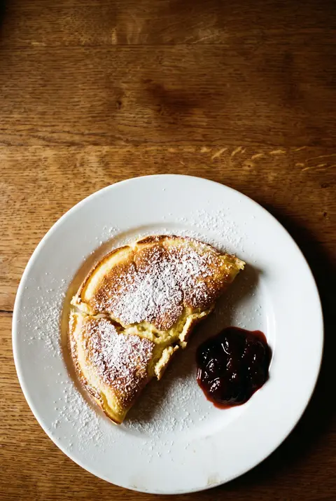 A portion of torn fluffy pancake dusted with powdered sugar on a white plate