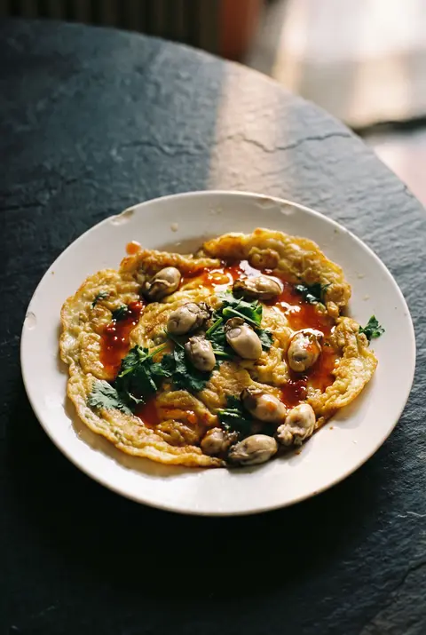 A plate of oyster omelette with small oysters on a white plate