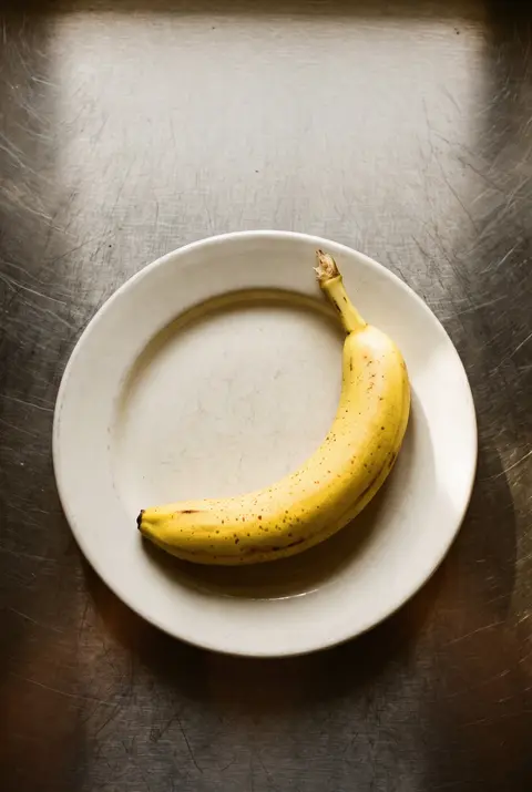 A ripe yellow banana with a few brown freckles on a white plate