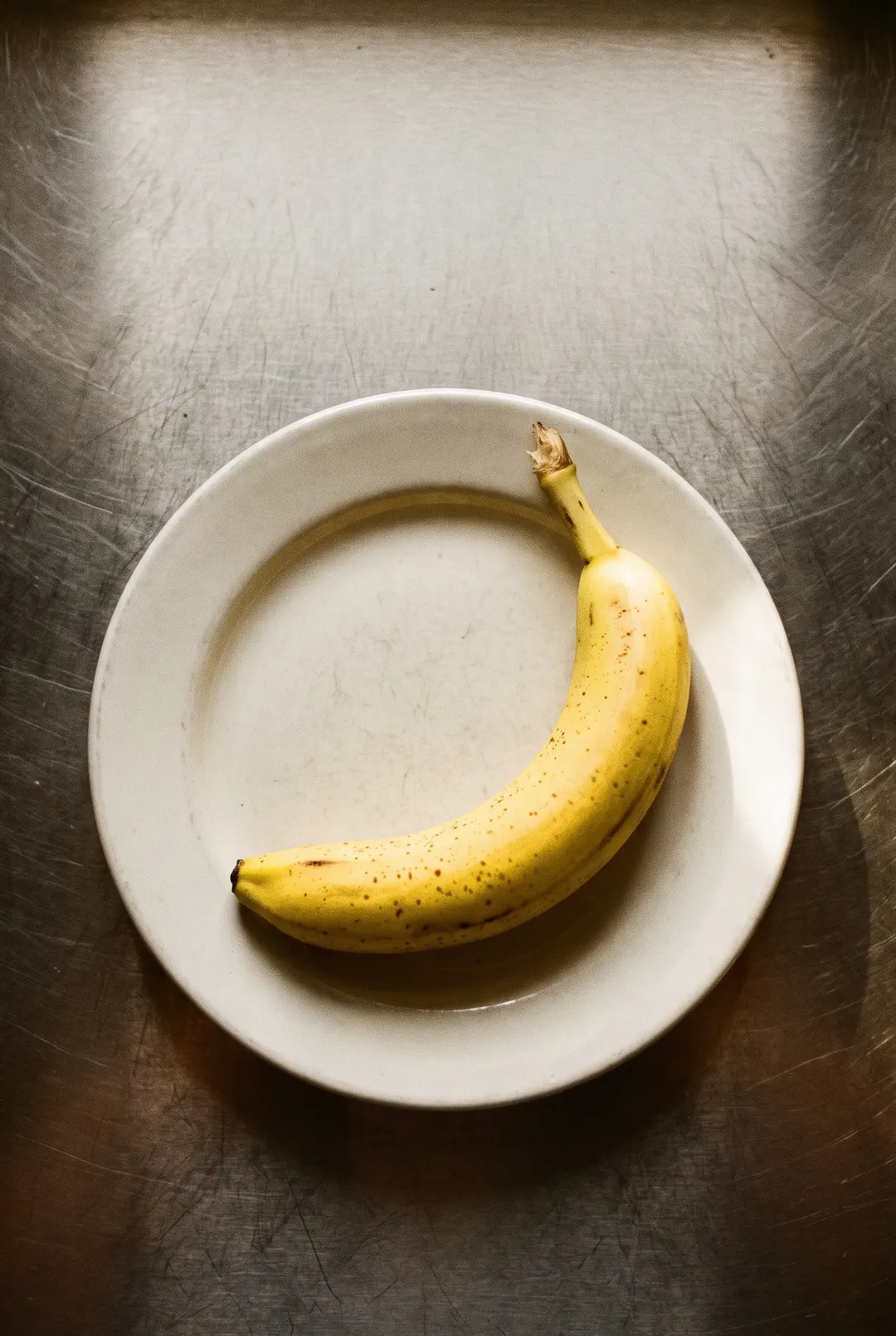 A ripe yellow banana with a few brown freckles on a white plate