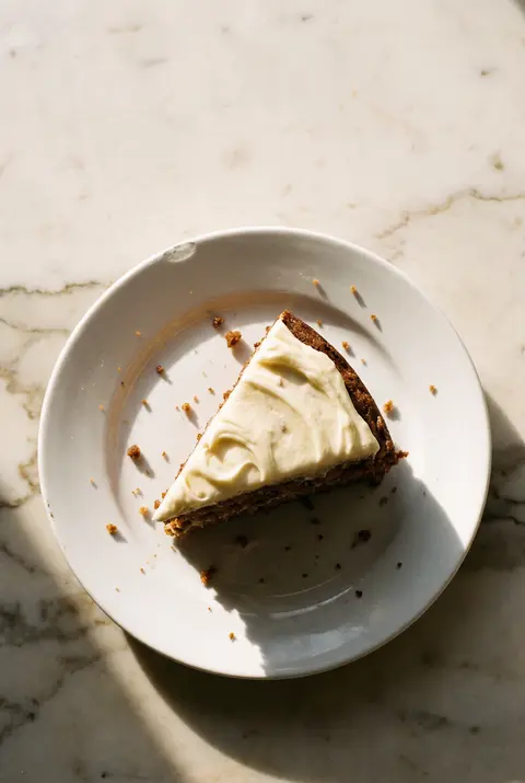 A slice of carrot cake with thick cream cheese frosting on a white plate