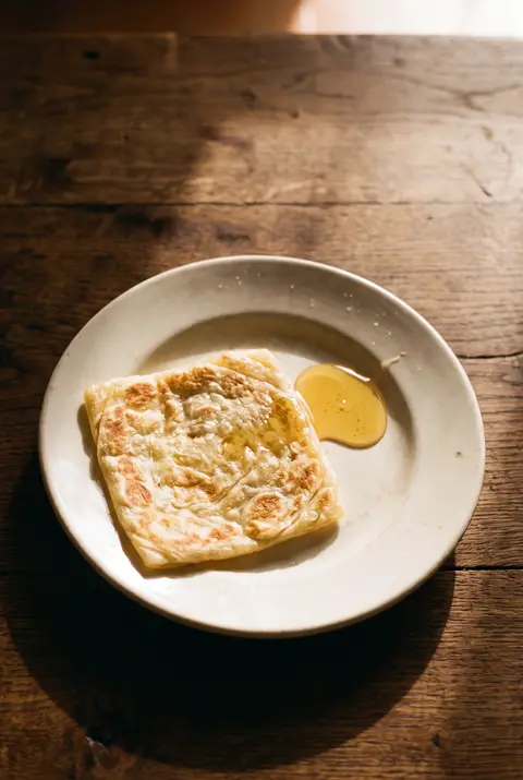 A square flaky msemen flatbread on a white plate
