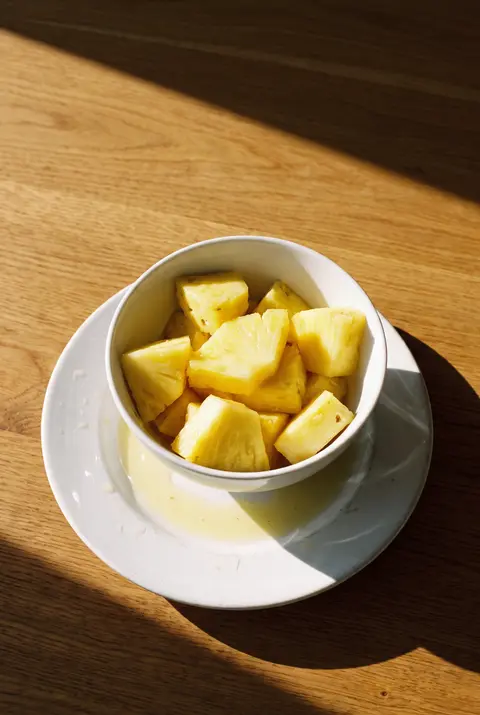 A white porcelain bowl of fresh pineapple chunks on a white plate