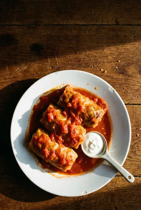 Three cabbage rolls filled with meat and rice in tomato sauce on a white plate