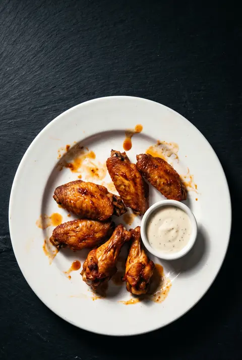 Six roasted chicken wings with a small dish of dip on a white plate
