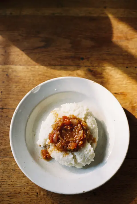 A plate of stiff white pap with a spoonful of tomato and onion relish on a white plate