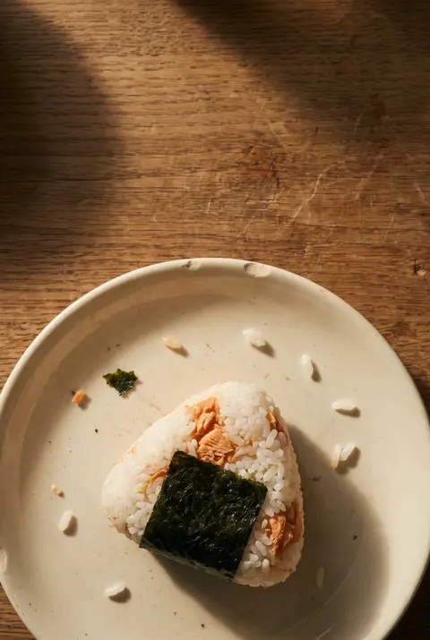 A triangle onigiri rice ball with salmon on a white plate