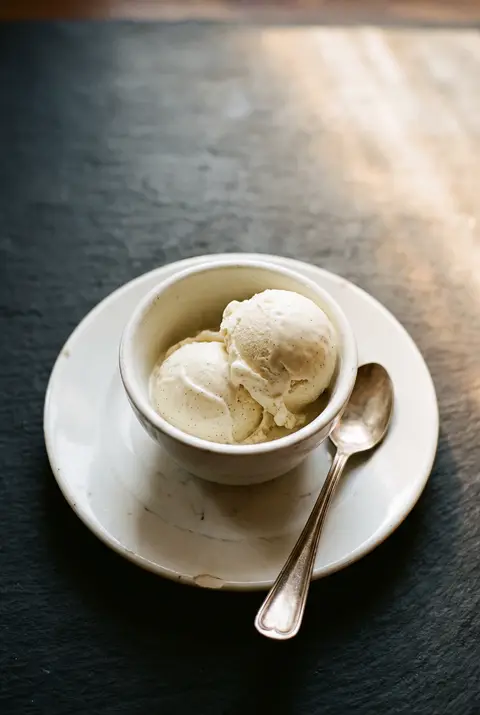 Two scoops of vanilla ice cream in a small white porcelain bowl on a white plate