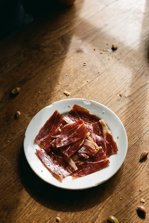 A tapas plate of thin slices of dark red jamon iberico on a white plate
