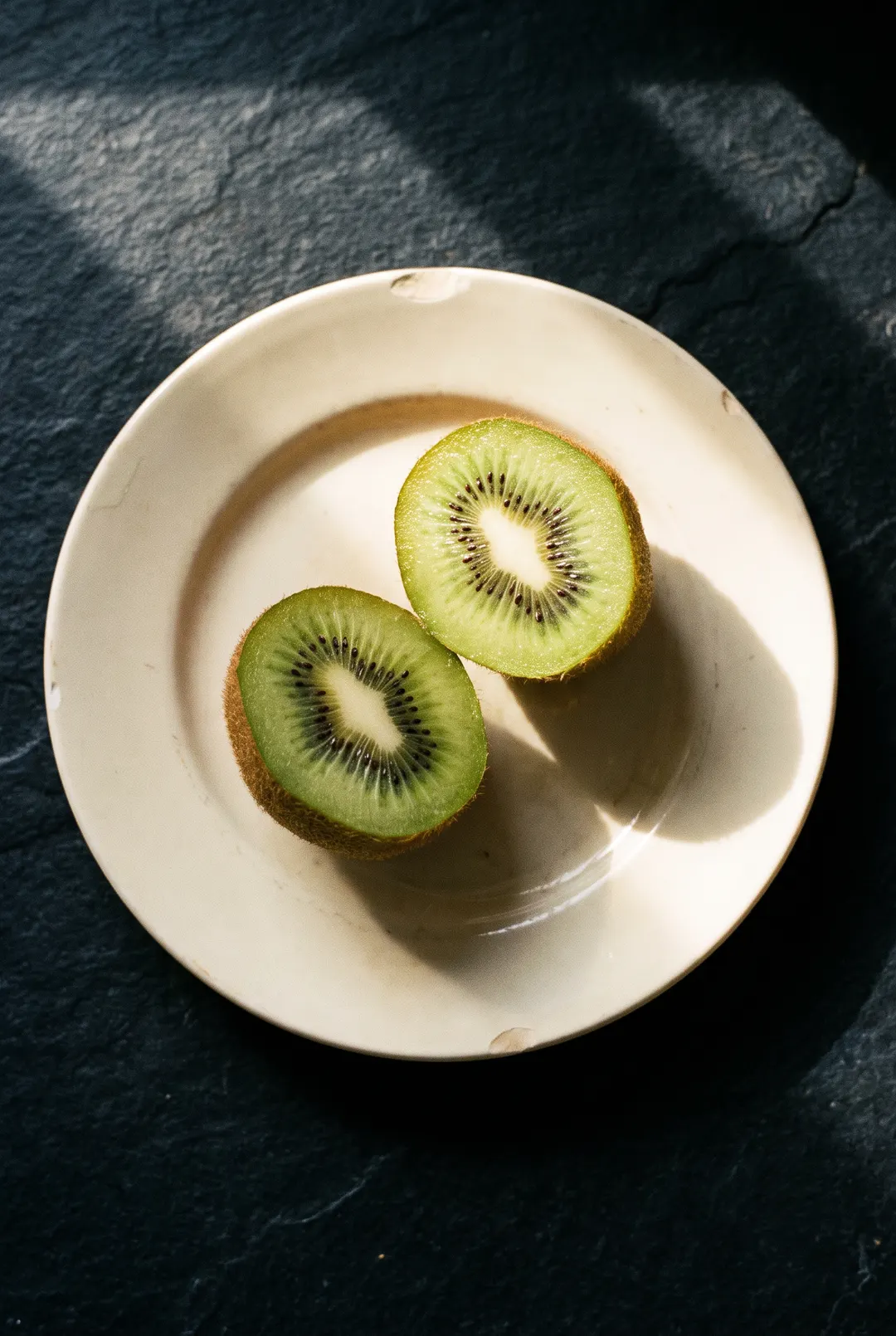 A kiwi cut in half showing the green flesh and black seeds on a white plate